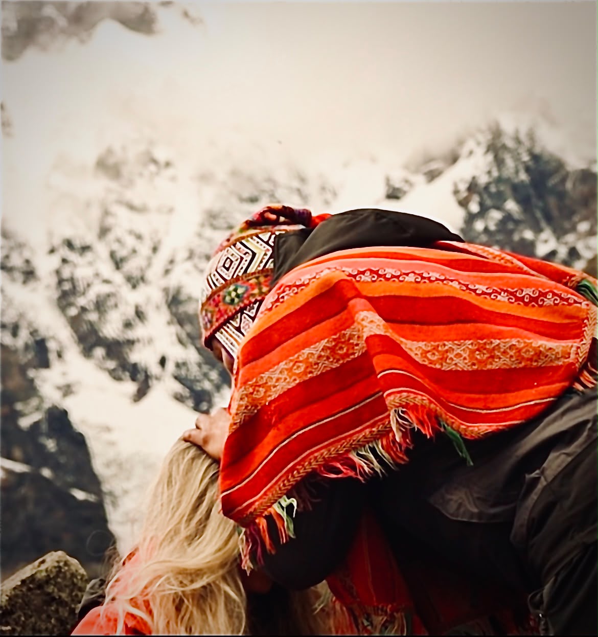 Paqo con poncho tradicional abrazando a una participante frente a una montaña nevada